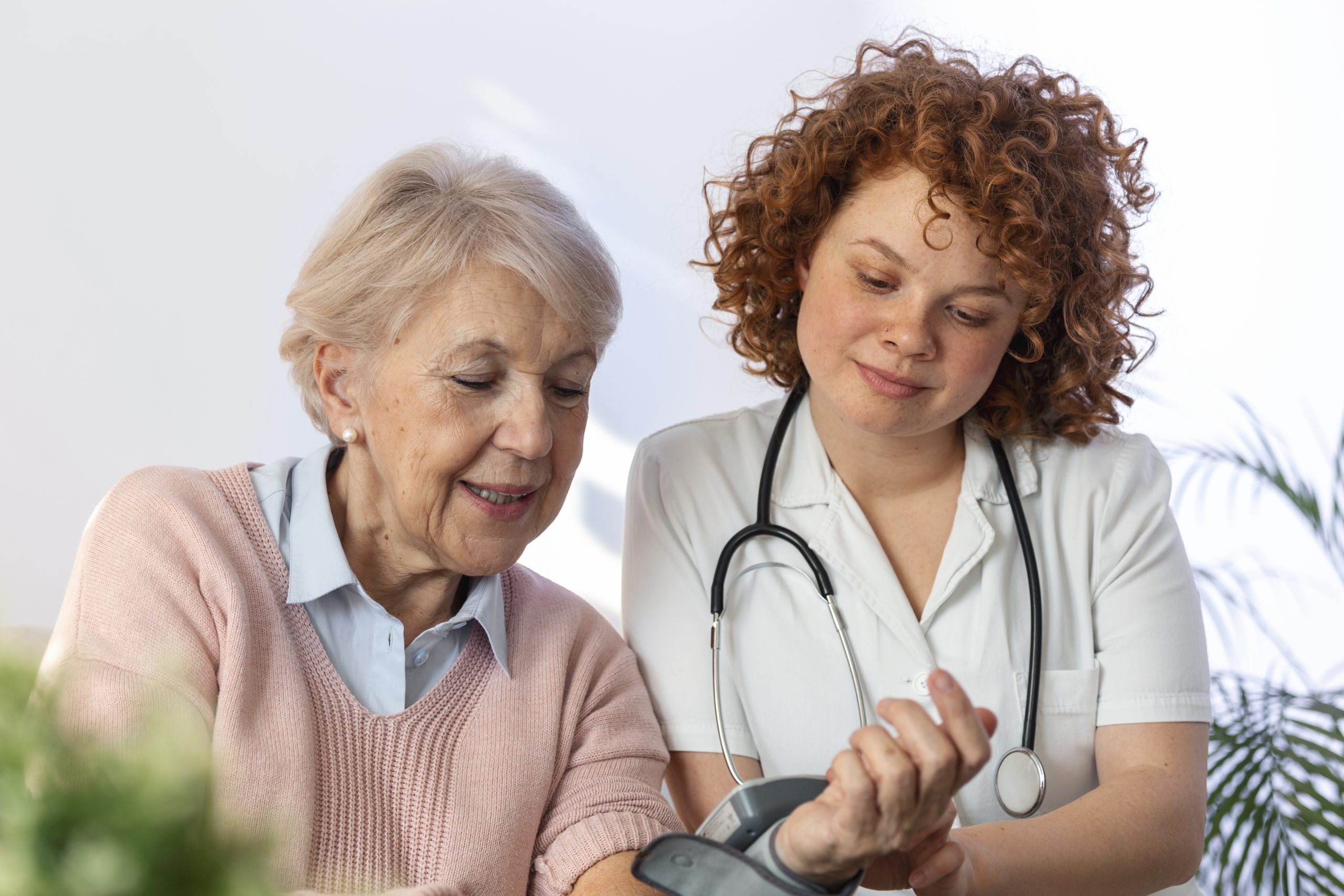 Caregiver measuring blood pressure of senior woman at home. Kind carer measuring the blood pressure of a happy elderly woman in bed in the nursing home.